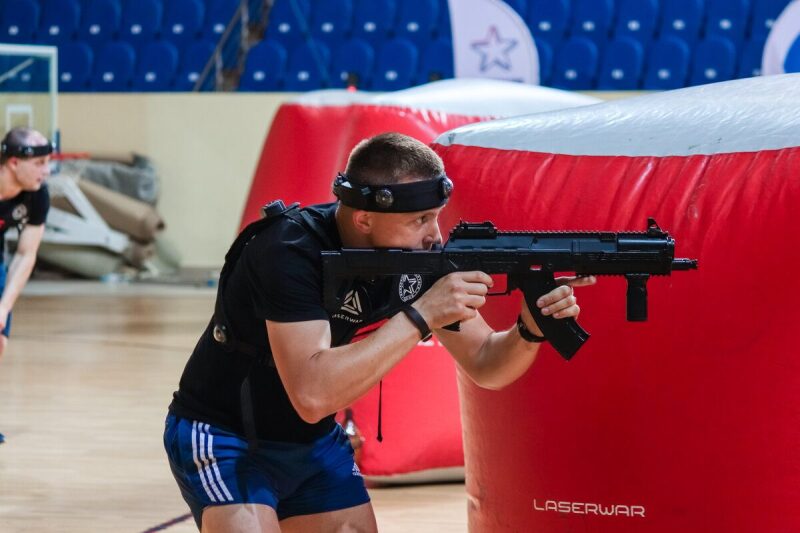 Игрок LASERWAR с автоматом держит оборону у красного укрытия.